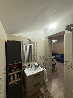 A bathroom with a sink, mirror, and towel rack. There is a shower area visible through a glass door. - Small house with a garden, parking space, gazebo, tables, chairs, and an outdoor kitchen. (Pagani)