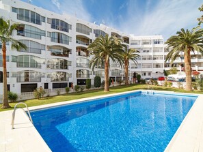 Ein modernes Hotel mit Swimmingpool, Palmen und blauem Himmel.