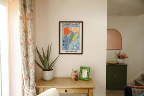 A room with a framed picture of a flower market, a potted plant, a small vase with flowers, and a cabinet. - New 3 Bed House | Stafford | Private Parking (Stafford)