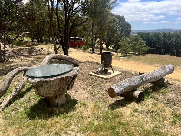 A rustic outdoor setting with a wooden table, a fire pit, and logs.