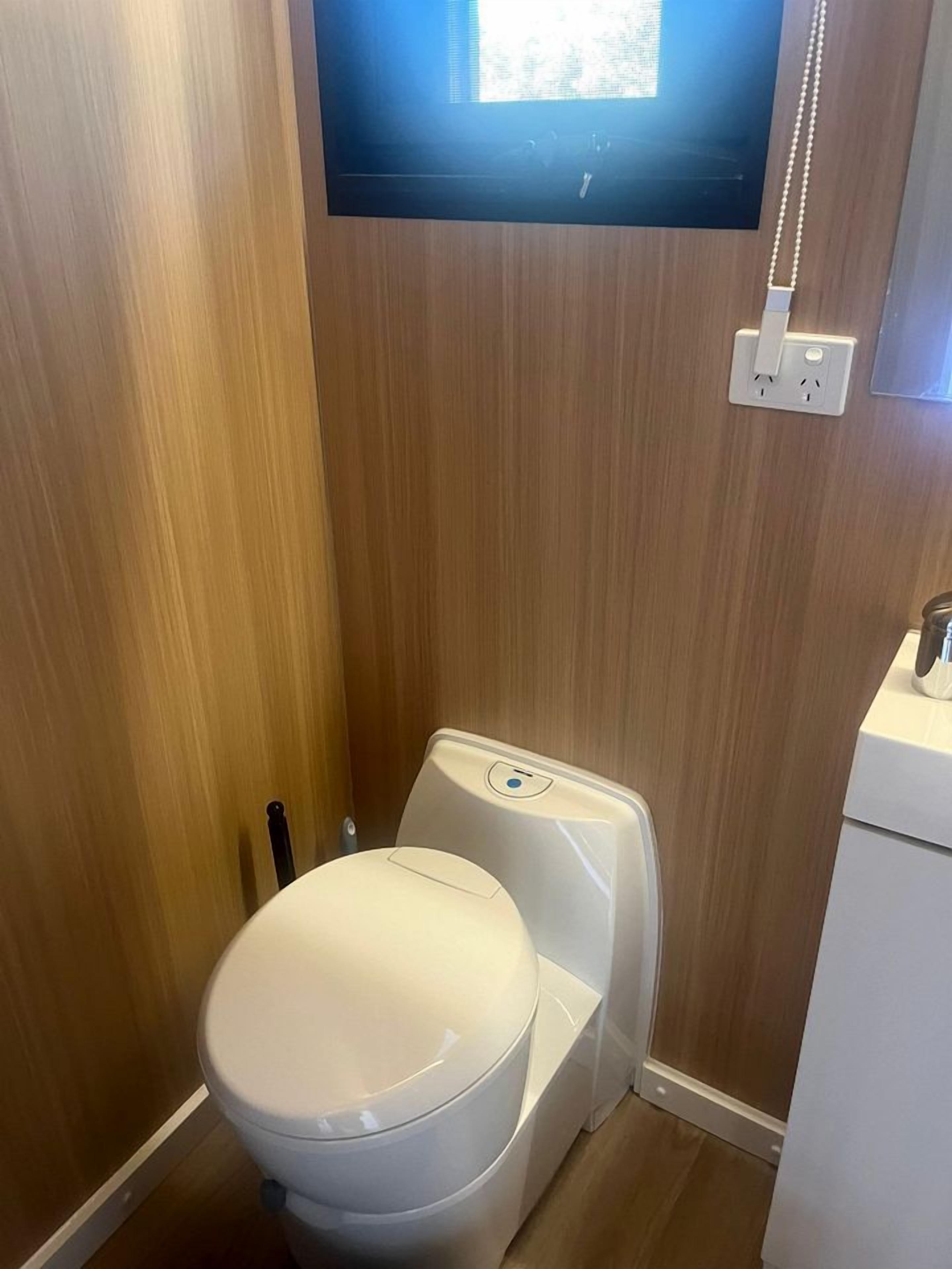 Ein kleines Badezimmer mit einer weißen Toilette, einem montierten Fernseher und einer Steckdose an der Wand.