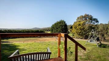 A wooden deck with a view of a grassy field and a swing set.