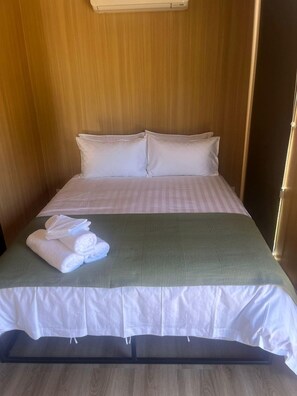 A hotel room with a bed, pillows, a green blanket, and rolled towels.