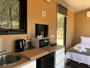 A compact room with a kitchenette, a bed with white linens, and a window with a view of trees.