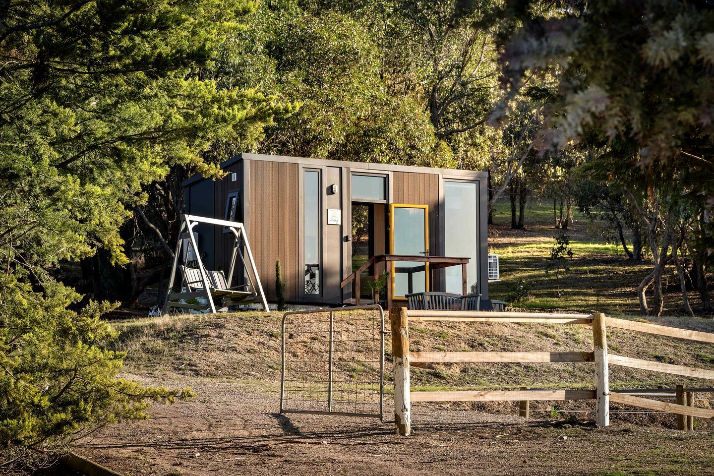 A modern cabin with a wooden exterior, a swing set, and a fenced area.