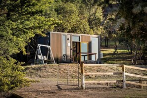 A modern cabin with a wooden exterior, a swing set, and a fenced area.