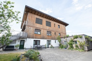 Ein mehrstöckiges Gebäude mit einem geneigten Dach, Holzfassade und einem gepflasterten Innenhof mit Außenbestuhlung.