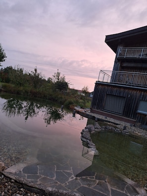 A serene lakeside setting with a wooden building featuring balconies. - Apartment 'Gemütliche Mit Schwimmteich' with Shared Terrace, Shared Garden and Wi-Fi (Kemating)