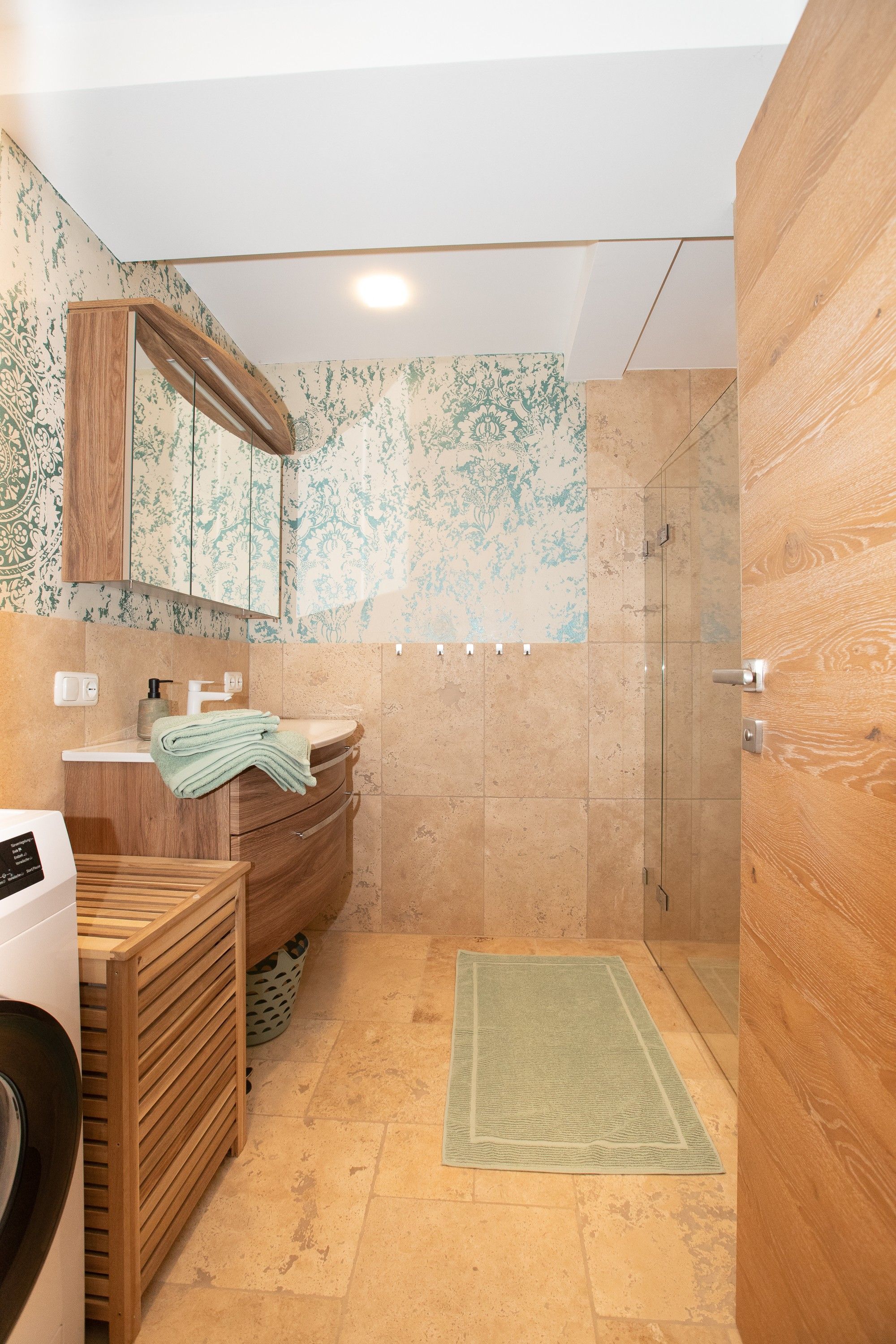 Ein modernes Badezimmer mit einem Holzkosmetikschrank, einer Glasdusche und einer Wand mit Muster.