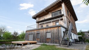 Un edificio de madera de varios pisos con balcones, una escalera y una zona de terraza.