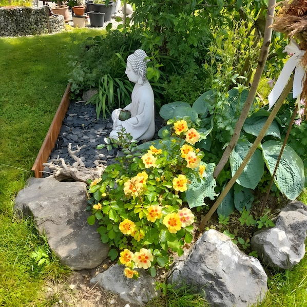 A garden with a Buddha statue, yellow flowers, and large green leaves.
