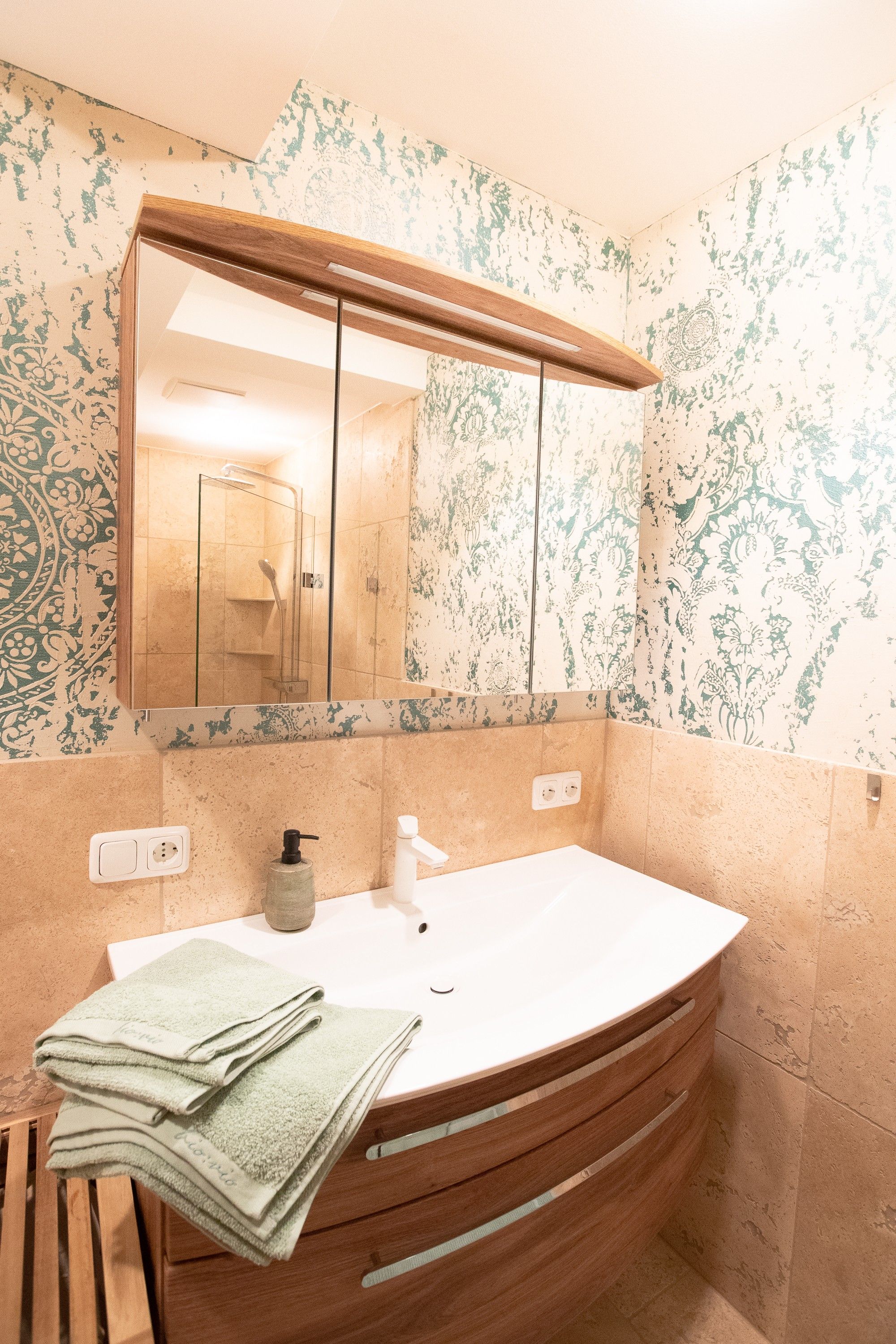 Een badkamer met een vrijstaand wastafelmeubel, een spiegel, een handdoekhouder en een douchegedeelte.