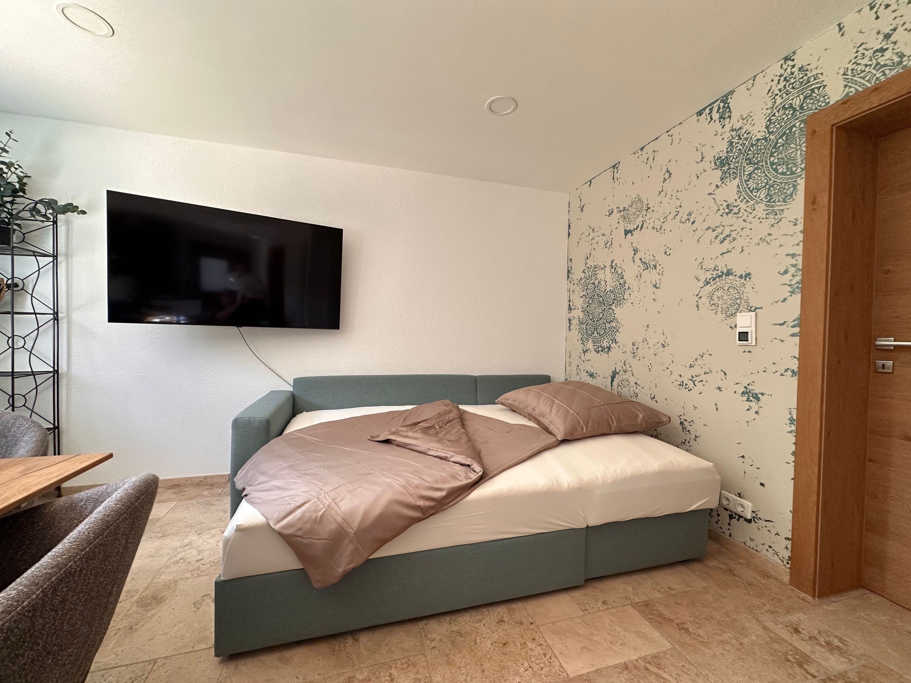 Quarto moderno com cama, televisão na parede e papel de parede estampado.