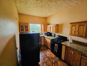 A kitchen with wooden cabinets, a black refrigerator, a stove, and a window with bars. - Awesome 6-bedroom building with AC in St. Ann Parish (St. Ann Parish)