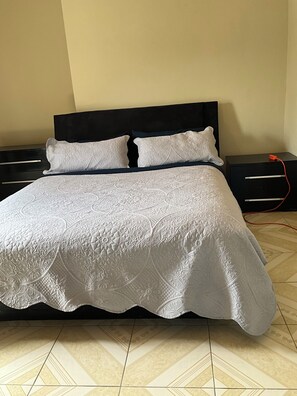 A bed with a patterned bedspread, two pillows, a black headboard, and a nightstand with a red cable. - Awesome 6-bedroom building with AC in St. Ann Parish (St. Ann Parish)