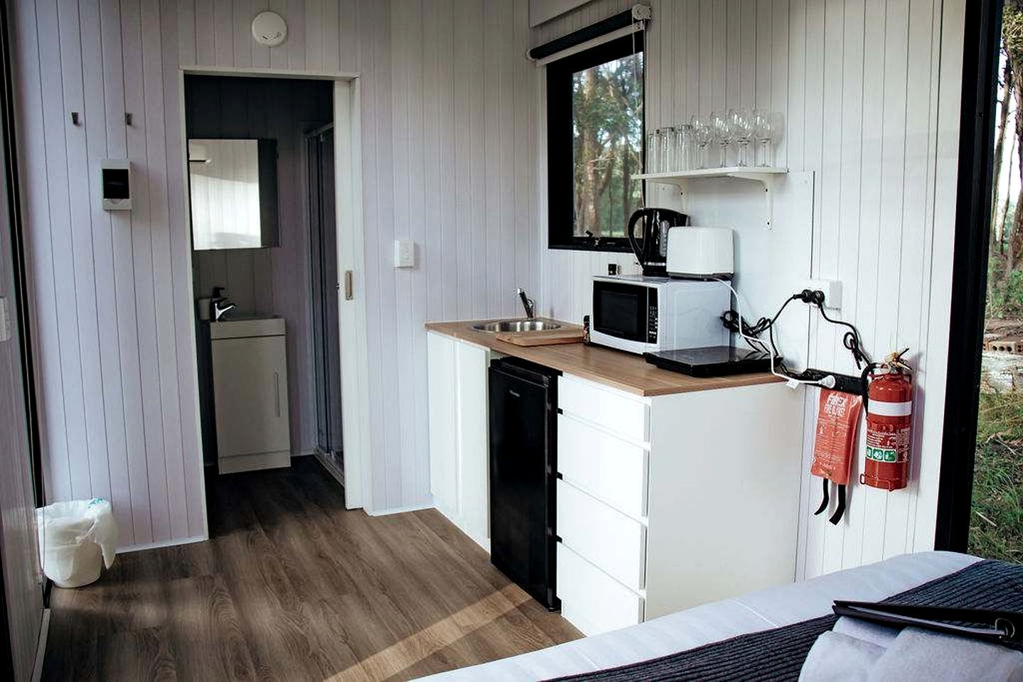 Een compacte keuken met een magnetron, spoelbak en een brandblusser aan de muur.