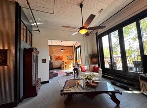 A spacious living area with a large window, a ceiling fan, and a fireplace. - Stay Downtown Hot Springs! Devine's Downtown (Hot Springs)