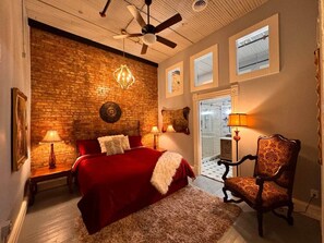 Un dormitorio con pared de ladrillo, cama con ropa de cama roja, candelabro y una silla.