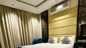 A hotel room with a large bed, a bedside table, a wardrobe, and a window with curtains. - Alrafahya Crown (Riyadh)