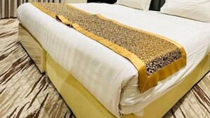 A hotel room with a large bed, a bedside table, an air conditioning unit, and a window with curtains. - Alrafahya Crown (Riyadh)