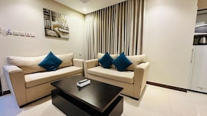 A living room with two beige sofas, a black coffee table, and a painting on the wall. - Alrafahya Crown (Riyadh)