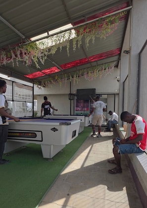 A pool table with players, a billiards table, and a red-roofed area with hanging plants. - Tayanne Stays (Nairobi)