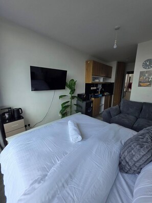 A hotel room with a bed, a TV mounted on the wall, a kitchenette, and a grey sofa. - Tayanne Stays (Nairobi)