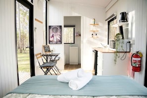 A cozy room with a bed, a small table with chairs, a kitchen area, and a view of the outdoors.