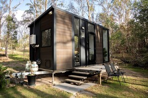A modern cabin with a deck, outdoor seating, and a gas cylinder.