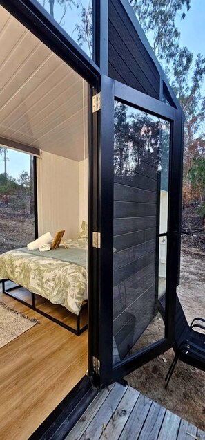 Une chambre moderne avec un lit, un plancher en bois et une grande porte-fenêtre coulissante donnant sur un espace extérieur.
