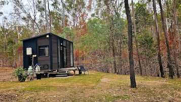 A small cabin with a deck, surrounded by trees in a forest setting.