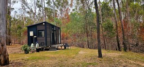 Una cabaña pequeña con terraza, rodeada de árboles en un bosque.