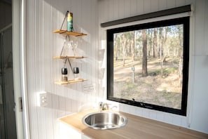 A kitchen with a stainless steel sink, wooden countertop, and a window with a forest view.