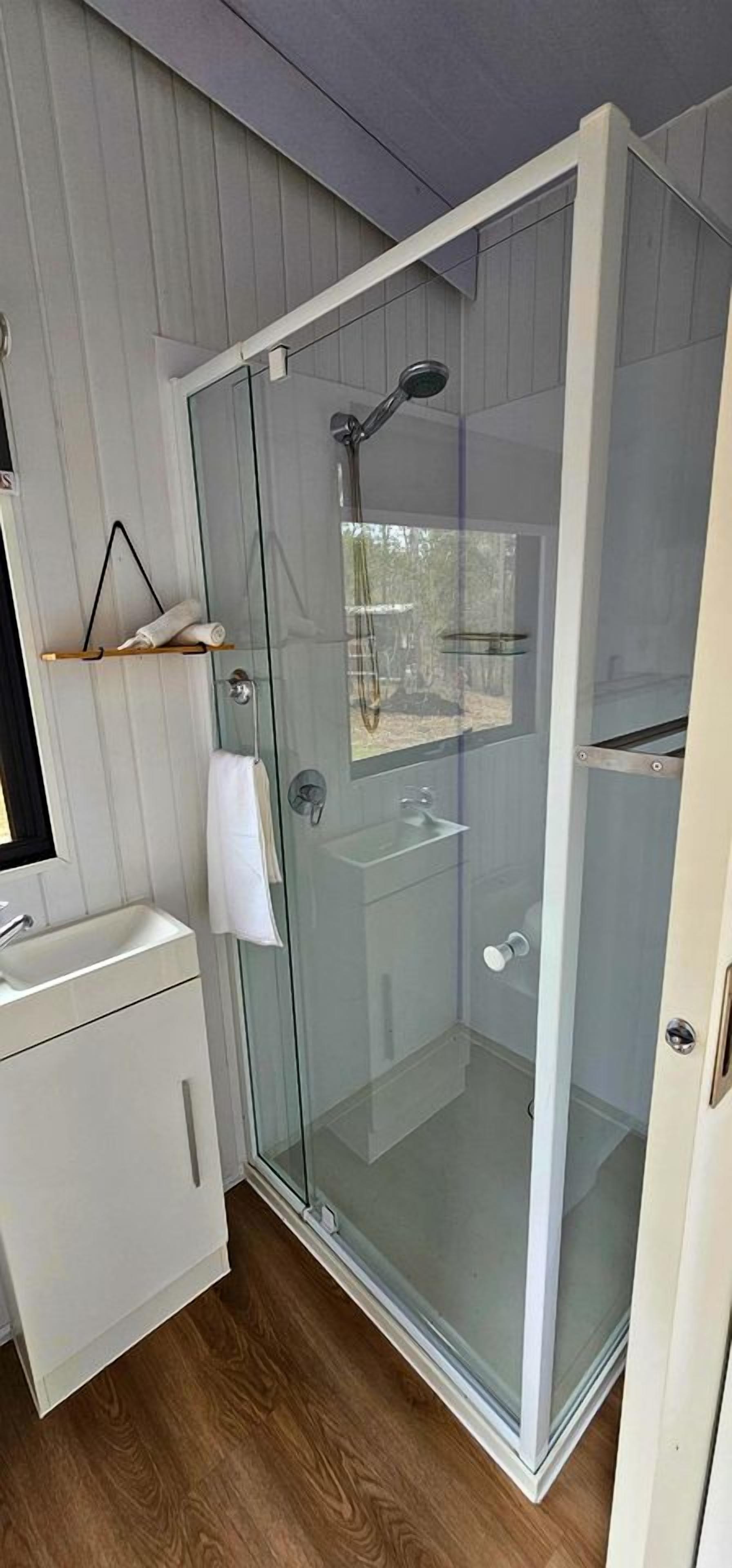 A glass-enclosed shower with a handheld showerhead, a white sink with a mirror, and a towel hanging on the wall.