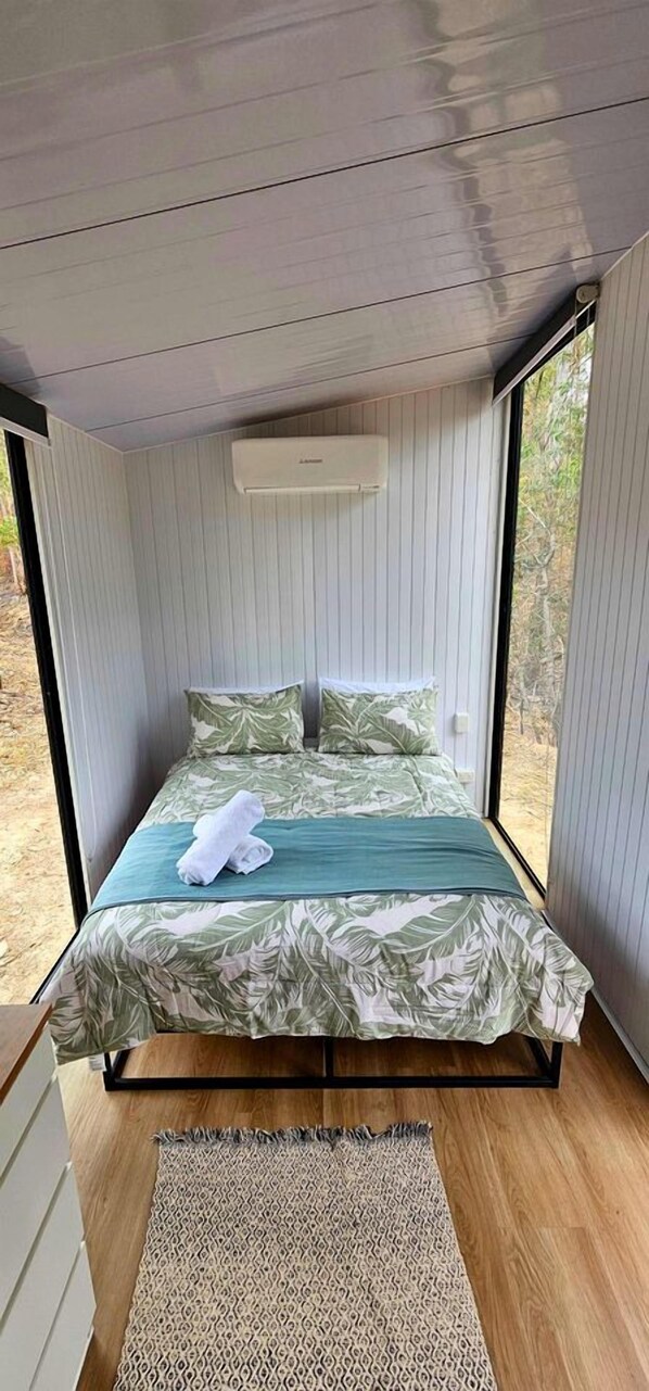 Una cama con un edredón estampado, una toalla blanca y un aire acondicionado instalado en el techo.
