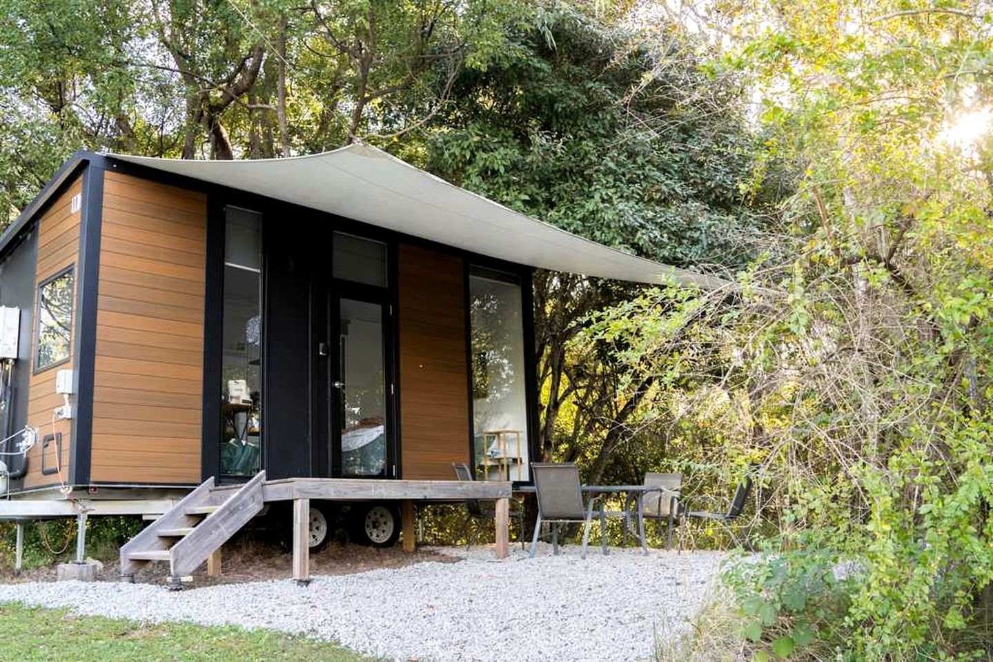 A modern cabin with a covered deck, large windows, and a gravel driveway.