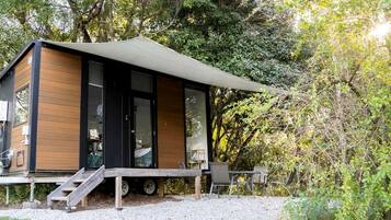 A modern cabin with a covered deck, large windows, and a gravel driveway.