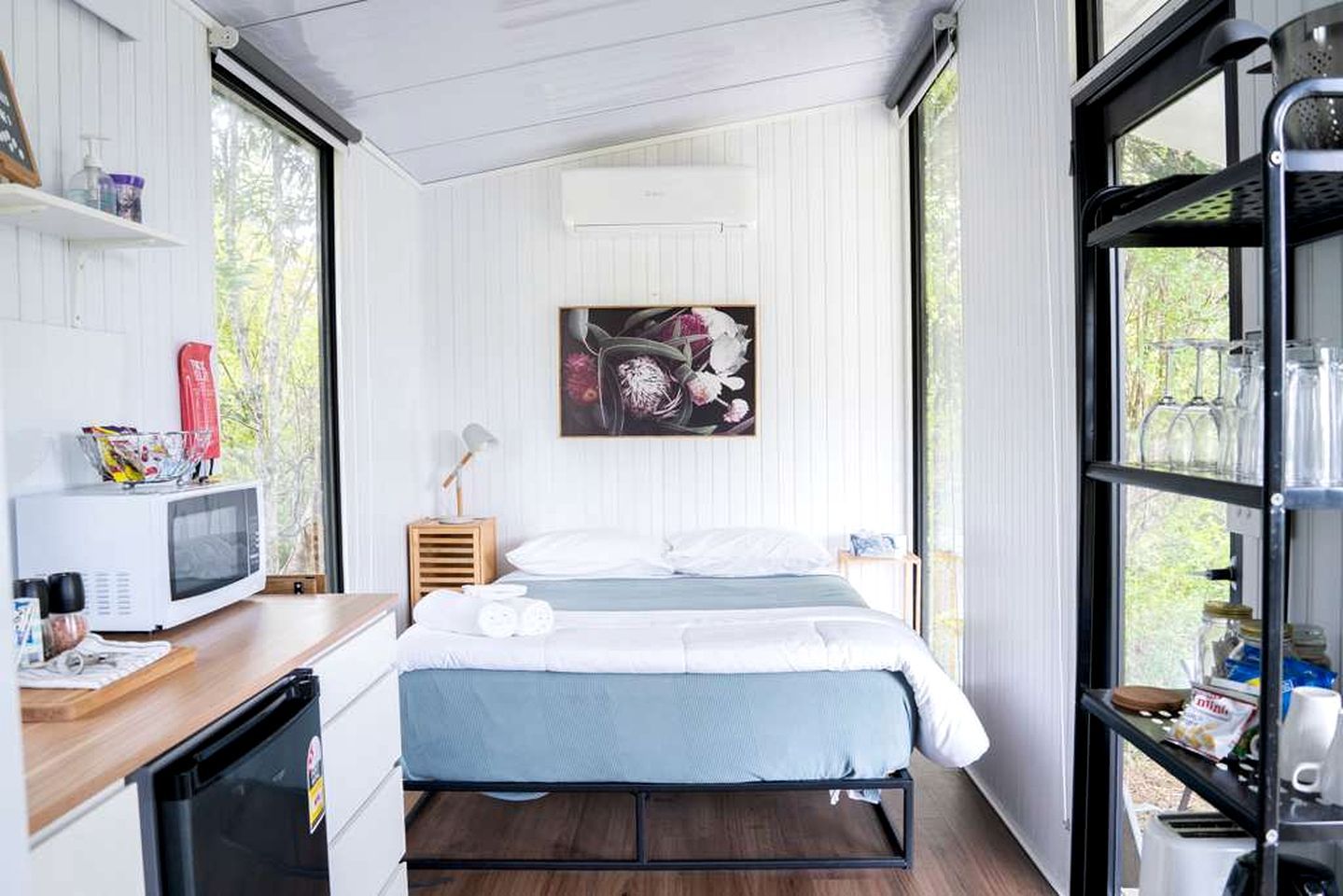 Une chambre compacte comprenant un lit, une petite table de chevet, un four à micro-ondes, un réfrigérateur et une fenêtre donnant sur un espace verdoyant.