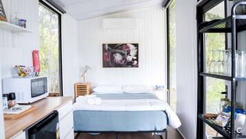 Une chambre compacte comprenant un lit, une petite table de chevet, un four à micro-ondes, un réfrigérateur et une fenêtre donnant sur un espace verdoyant.