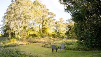 A grassy outdoor area with two chairs and trees in the background.