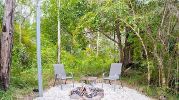 An outdoor seating area with two chairs and a small table, surrounded by trees and a fire pit.