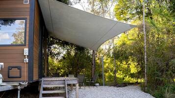 A wooden cabin with a covered patio, outdoor seating, and a gravel ground.