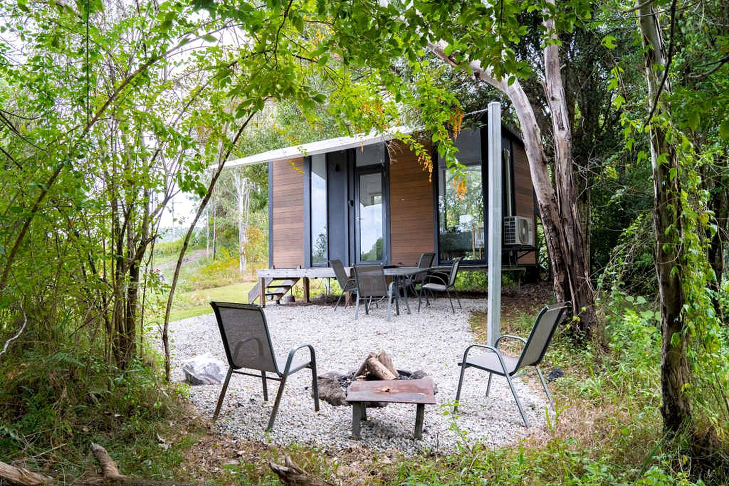Un espace extérieur moderne aménagé avec une table et des chaises, entouré d’arbres et bordé d’un bâtiment doté de grandes fenêtres.