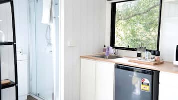 A modern kitchen with a dishwasher, a window with a view of trees, and a glass shower enclosure.