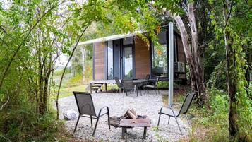 A modern outdoor seating area with a table and chairs, surrounded by trees and a building with large windows.