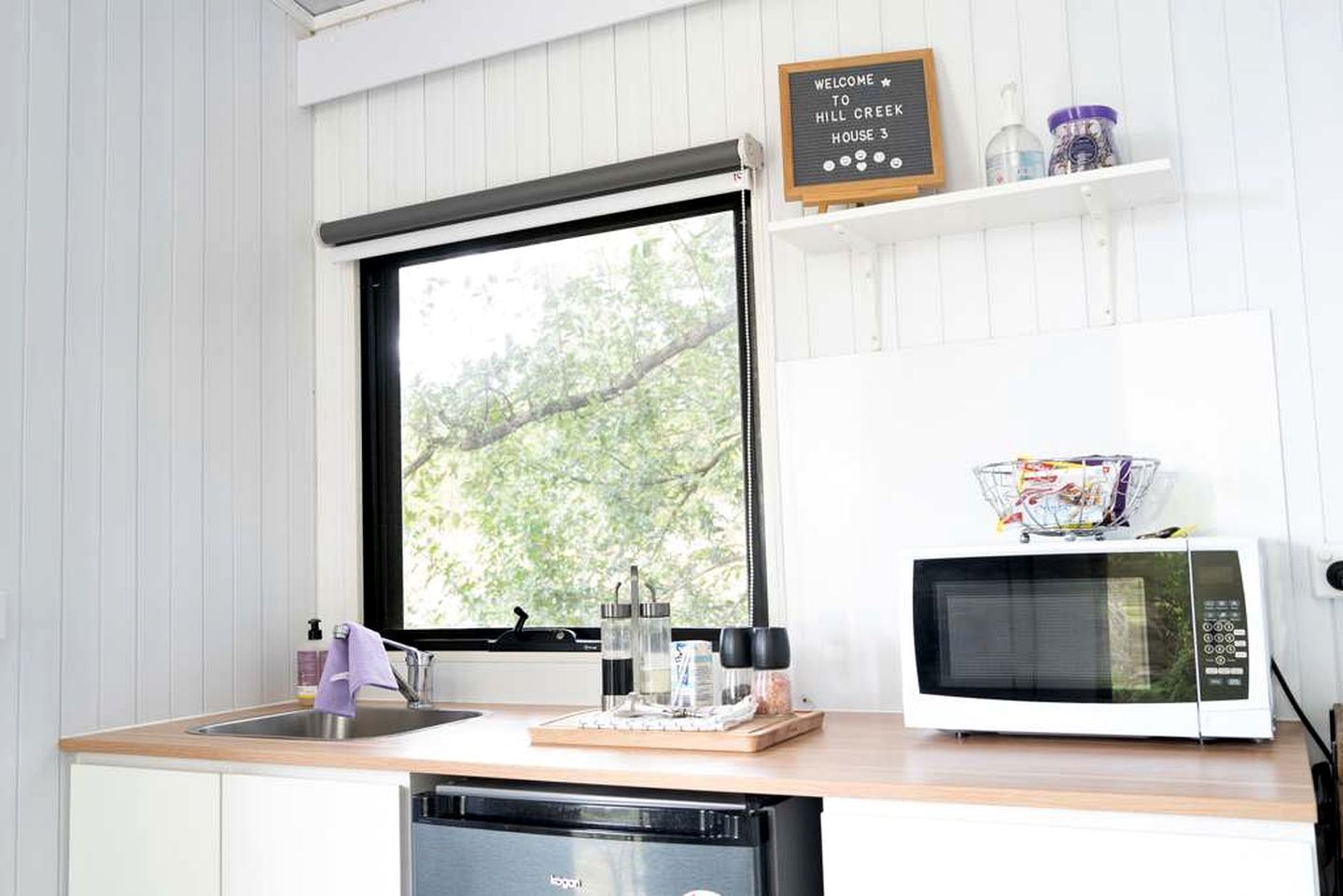 A kitchen with a window, a microwave, a sink, and a welcome sign.
