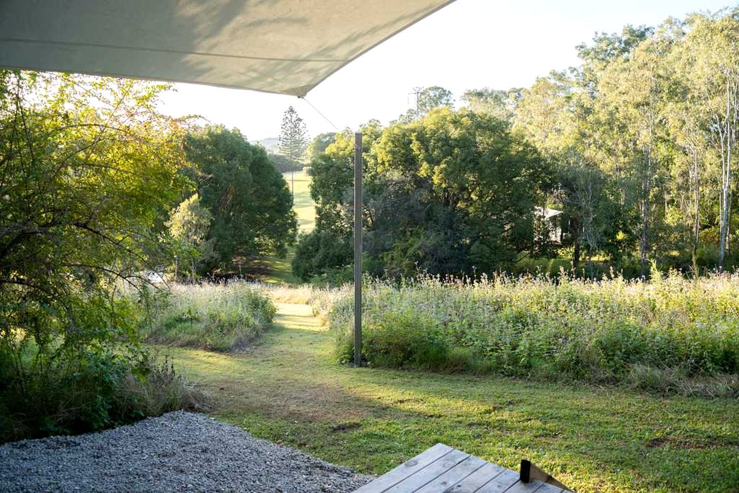 A covered outdoor area with a gravel path leading to a grassy area, surrounded by dense trees and vegetation.