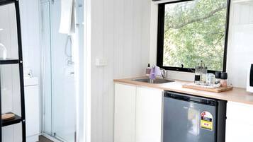 A modern kitchen with a dishwasher, a window with a view of trees, and a glass shower enclosure.