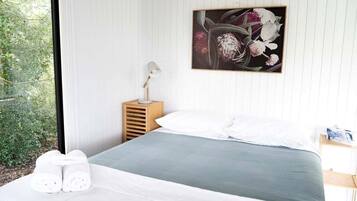 Ein Schlafzimmer mit einem Bett, Kissen, einem Nachttisch mit Lampe und einem gerahmten Blumenbild an der Wand.