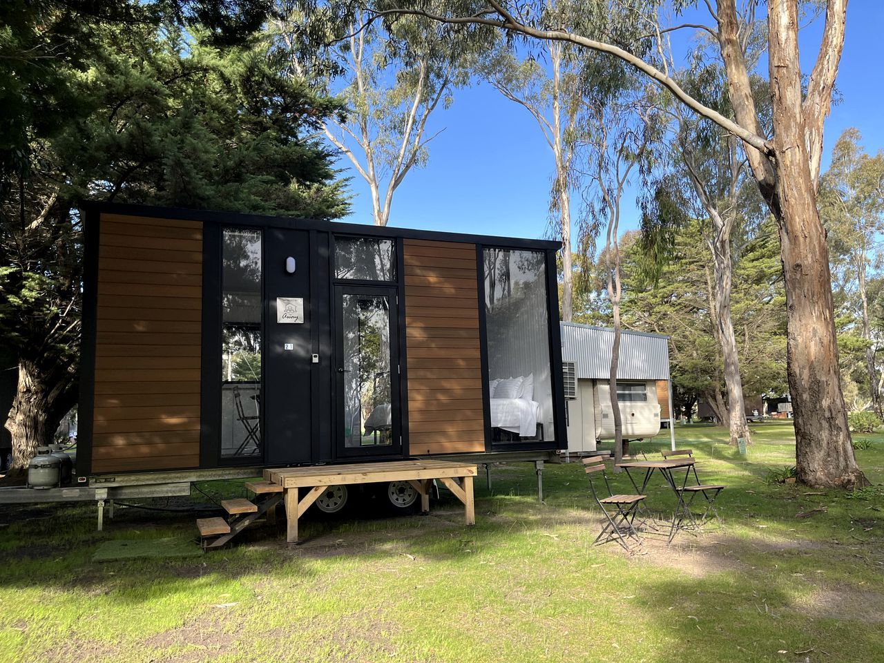 Un moderno e compatto camper con esterno nero e dettagli in legno, immerso in un'area erbosa con alberi sullo sfondo.